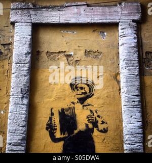 A graffiti of a dead accordionist decorates a yellow sealed wall in Guanajuato, Mexico Stock Photo