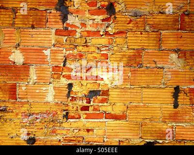 Detail of a colorful orange and yellow brick wall that has been repaired with odd shaped brick on the outside of a building. Stock Photo