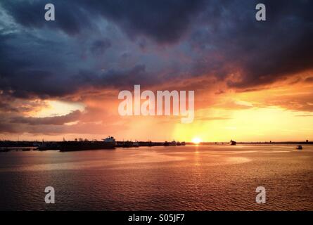 Dark, threatening rain clouds during Sunset over Southampton Water. Fawley Refinery is seen on the left Stock Photo