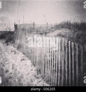 An old wooden beach fence runs along the sand dunes Stock Photo