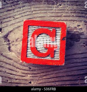 It's a woodblock toy with an alphabet letter on it: G Stock Photo