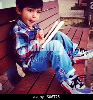 Little cheecky boy sit on a bench to read a book Stock Photo