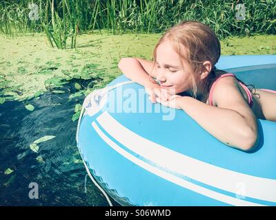 Little girl sitting in a raft on a river with lush greenery Stock Photo