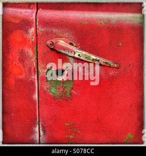 Red paint is peeling off revealing green underneath on the door of an old abandoned vintage truck Stock Photo