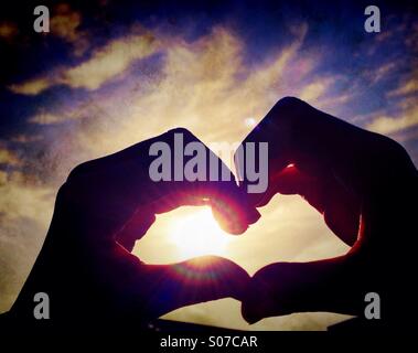 Child's hands forming heart shape against sun Stock Photo