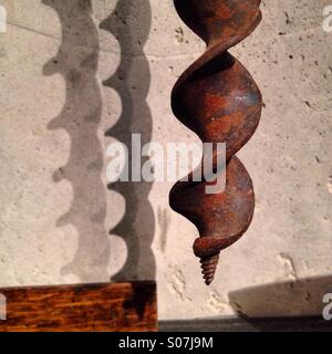 A very old rusty drill bit hanging on the wall in a workshop casting shadows Stock Photo