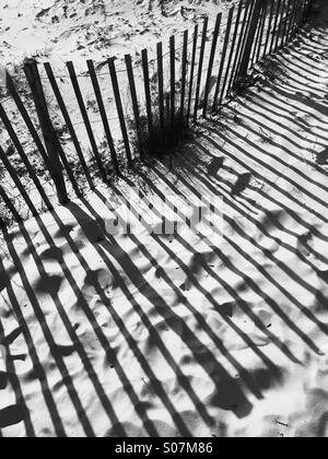 Shadows of a wooden beach fence in a  sand dune, in black and white. Stock Photo