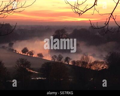 The view of the river Thames from Richmond Hill, Surrey, at sunset on a misty foggy autumn evening in November. The fading sun light illuminates the mist. Stock Photo
