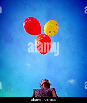 Girl blowing to keep three balloons up in air Stock Photo