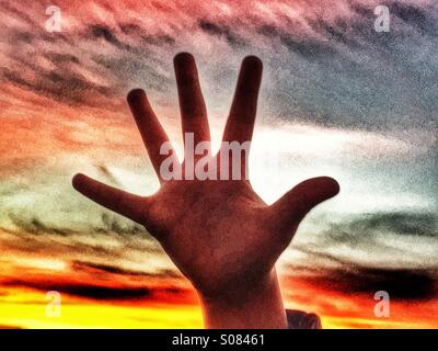 Child's hand against sunset Stock Photo