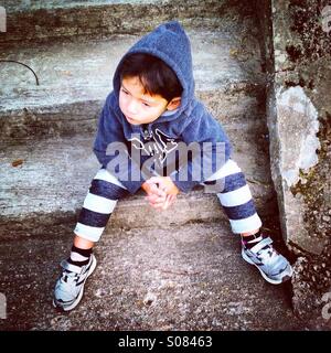 Little urban boy is sitting on the stairs in the street Stock Photo