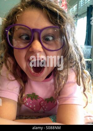 Young girl wearing big glasses and front teeth missing and playing cross eyed. Stock Photo