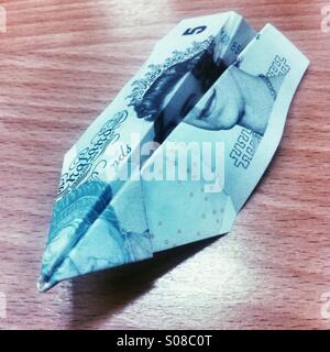 Five pound note folded into a paper plane Stock Photo