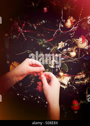Young girls hands putting decorations on Christmas tree Stock Photo