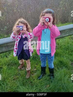 Two young children using digital cameras taking photos. Stock Photo