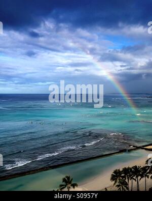 Rainbow over the Pacific Ocean in Waikiki, Hawaii. Surfers scattered in the water are like little specks. Stock Photo