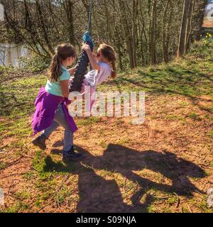 Two girls playing on a rope swing Stock Photo