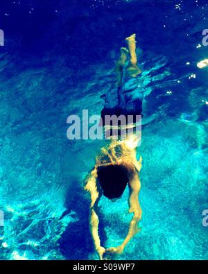 Young man swimming underwater in swimming pool as the sun glistens through the water. Stock Photo