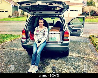 Teenage girl leaving home to go to college sitting in the car near boxes Stock Photo