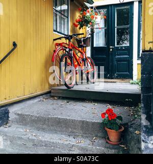 Red Bicycles parked outside typical yellow painted wooden building on Vaxholm, Stockholm archipelago, Sweden with pot with red geraniums in foreground Stock Photo