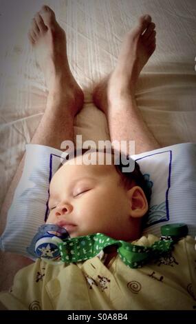 Beautiful baby girl sleeping on her father's legs Stock Photo