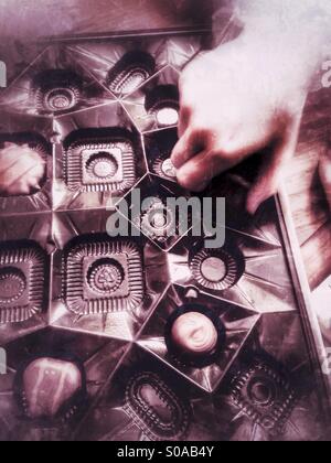 A child picking up candy from a box of chocolates. Stock Photo