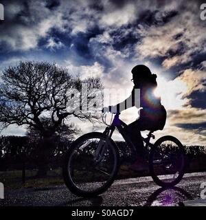 Young girl cycling in front of the sun Stock Photo