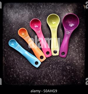 Five coloured measuring spoons against a black marble work surface. Stock Photo