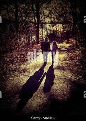 Mother and daughter walking holding hands down country path casting long shadows
