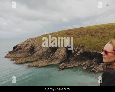 Girl / woman in red sunglasses looking out over headland into the sea ocean Stock Photo