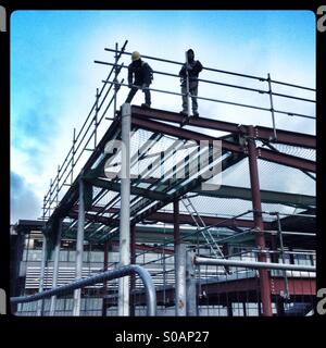 Builders putting up a scaffolding around a steel frame Stock Photo