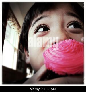 A six year old Asian Caucasian mixed race boy takes a bite of a cupcake. Stock Photo