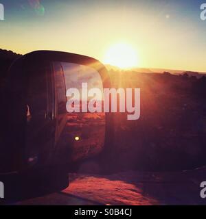 The sunset over Fins -n-Things off-road trail in Moab, UT reflects in a Jerp's rearview mirror. Stock Photo