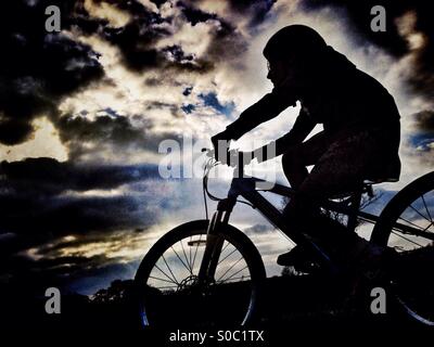 Young girl on bike in silhouette against dramatic sky