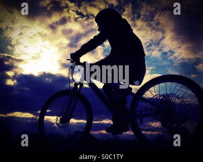 Young girl on bike in silhouette against dramatic sky