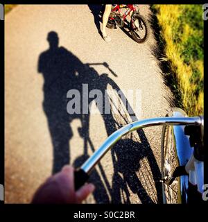 A shadow of a bike rider on a bike path talking to a child riding a bike. Stock Photo
