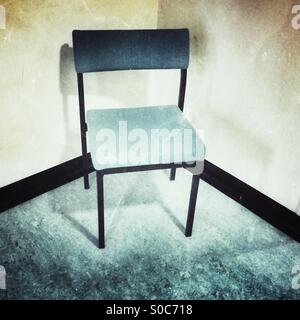 Lone single seat chair positioned in corner of empty room Stock Photo