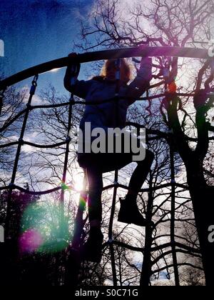 Young girl on climbing frame backlit by sun Stock Photo