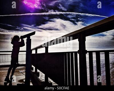 Young girl in silhouette using telescope at end of pier Stock Photo