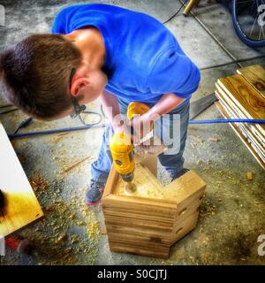 Young boy drills a hole in a wooden birdhouse Stock Photo