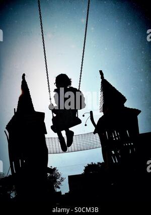 Young girl on swing in silhouette with fairytale castle in background. With dusk atmosphere and starry sky Stock Photo