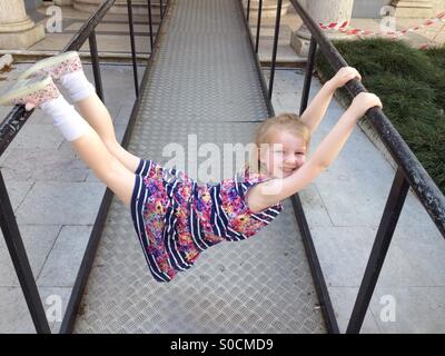 Happy child girl hangs on bars by her finger tips and toes Stock Photo