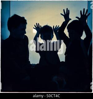Three children silhouettes playing with hands up Stock Photo