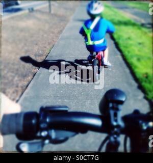 Child riding bicycle sidewalk wearing safety vest Stock Photo