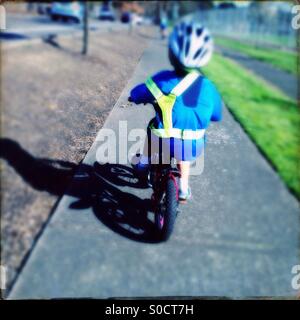 Child riding bicycle on sidewalk wearing reflective safety vest and bike helmet Stock Photo