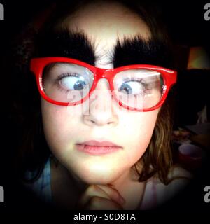 Young girl wearing red glasses with fake bushy eyebrows Stock Photo