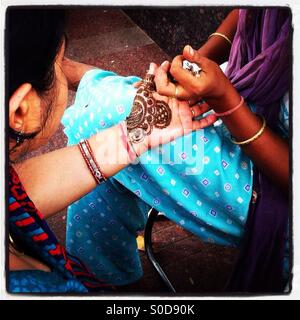 A woman has her hand painted with henna by a street artist. Delhi, India. Stock Photo