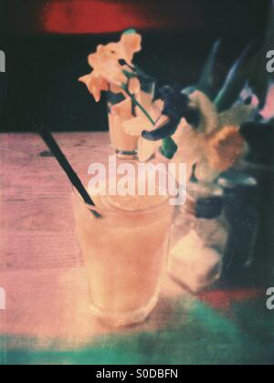 Glass of fresh squeezed fruit juice on cafe table with flowers, daffodil and iris, in misty vintage style Stock Photo