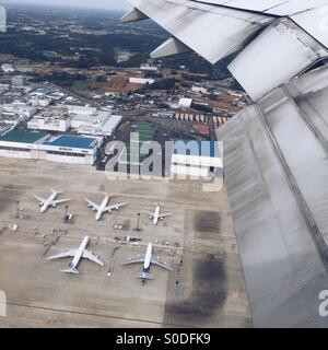 Aerial view of airplane wing, warehouses and airplanes on the ground at Narita International Airport in Chiba Prefecture, Japan, as seen from plane window. Stock Photo