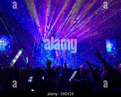 Hands and glow sticks in the air as confetti rain down in a burst of color at the end of a concert. Stock Photo